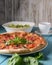 Fresh italian pizza with salami and black olives and other food on the background. Blue colored wooden table