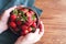 Fresh juicy strawberries in a clay round plate in female hands on a wooden table background, close-up