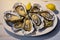 Fresh large oysters, beautifully presented with lemon slices, on a pristine white plate, an exquisite seafood delicacy