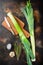 Fresh leek stalks with herbs ingredients for cooking Braised Leeks, onrustic metall background dark, top view with  space for text