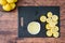 Fresh lemon juice in a white bowl, lemon halves on a black cutting board, wood table, basket of lemons