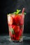 Fresh lemonade with ice, mint and strawberry on top in glass on black table background. Cold summer drink. Sparkling glasses with