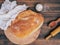 Fresh loaf of bread covered with a white cloth near salt on old boards background. Composition with bread, salt, cloth