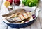 Fresh mackerel fish baked with a lemon, bow, salt and pepper on a wooden table