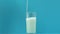 Fresh milk pouring in glass on blue background, source of calcium and phosphorus