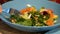 Fresh mixed salad with leafy greens and vegetable in blue ceramic bowl, eating at restaurant with metallic fork.