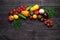Fresh multi-colored vegetables rich in vitamins on a dark wooden background are located in the middle in the shape of a branch.