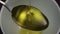 Fresh olive oil fills a metal spoon and flows into a gray bowl in slow motion.