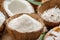 Fresh opened coconuts along with coconut slices, flakes and coconut leaves on a wooden table