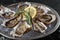 Fresh opened oysters, ice and lemon on a round metal plate, black stone textured background. Side view with copy space