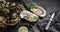 Fresh opened oysters with lemon, spices, salt, a knife and seaweed on slate stone background. Seafood, Shellfish, close up