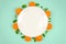 Fresh orange fruits and mint leaves on top view with white plate and pastel green color background for healthy food concept