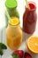 Fresh orange, strawberry and broccoli smoothie in bottles with fruits and vegetables on a white wooden rustic background, closeup