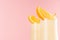 Fresh oranges milkshake with pieces juicy citrus, striped straws detail, closeup, top section on pink background.