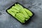 Fresh organic mangetout, also known as sugar snap pea, in plastic container, on gray stone background