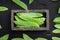 Fresh organic mangetout, also known as sugar snap pea, in wooden box, on black stone background, top view flat lay