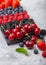 Fresh organic summer berries mix on black marble board on light kitchen table background. Raspberries, strawberries, blueberries,