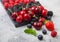 Fresh organic summer berries mix on black marble board on light kitchen table background. Raspberries, strawberries, blueberries,