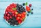 Fresh organic summer berries mix in white plate on blue wooden table background. Raspberries, strawberries, blueberries,