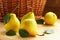 Fresh pears with green leaves in front of wattled basket on wooden background