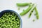 Fresh peeled green sugar snap peas in a bowl and open pods on a white wooden table background with copy space.