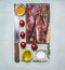 Fresh pieces of raw lamb on a chopping board, with herbs, spices, cherry tomatoes, lined rectangle on wooden rustic background top