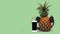 fresh pineapple with black headphones and smartphone with  black screen against green background
