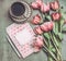 Fresh pink pale tulips flowers with heart letter , blank paper , marker and cup of coffee , top view.