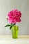 fresh pink peony in green transparent glass vase on wooden table