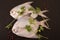 Fresh pomfret garnished with peppercorns and coriander on black background.