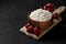 Fresh pure homemade cottage cheese in a wooden plate with strawberries on a black table, healthy food against a dark background