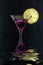 Fresh Purple rain cocktail in a martini glass with ice and lemon slice on a black textured surface, reflected in water