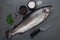 Fresh rainbow trout on dark stone table with salt, pepper and knife.