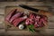 fresh raw beef meat cut into pieces in the process of cooking lies on a wooden cutting board with a kitchen knife, herbs and