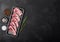 Fresh raw butchers lamb beef cutlets in plastic tray with fresh rosemary on black background.Salt, pepper and oil in steel bowl.