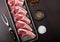 Fresh raw butchers lamb beef cutlets in plastic tray with vintage meat fork on brown background.Salt, pepper and oil in steel bowl