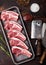 Fresh raw butchers lamb beef cutlets in plastic tray with vintage meat hatchets on black background.Salt, pepper and oil in steel