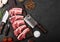 Fresh raw butchers lamb beef cutlets on stone board with vintage meat fork and knife and hatchet on black background.Salt, pepper