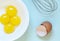 Fresh raw chicken yolks with whisk, eggs shells on the blue background. Baking or food preparation concept