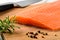 Fresh raw chilled salmon fillet, sharp knife, pepper grains and rosemary on a brown wood cutting board. Healthy eating, seafood