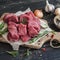 Fresh raw chopped beef on an olive board, spices, herbs and vegetables on dark wooden background.