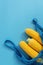 Fresh raw corn on the cob in a cotton mesh bag on a blue background. Flat lay, top view, copy space