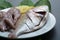 Fresh raw fish on white plate with green leaf and lemon