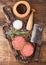 Fresh raw minced pepper beef burgers on vintage chopping board with mortar and pestle and meat hatchet on wooden background. Top