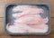 Fresh raw monk fish fillet on a black plastic tray on a wooden table. Retail industry product. Fishmonger craft . Premium price