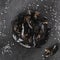 Fresh raw mussels in fishing net with seaweed and salt on slate stone over dark background. Seafood, Shellfish, top view, flat lay