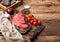 Fresh raw organic slice of braising steak fillet on chopping board with meat hatchet on wooden background. Red onion, tomatoes