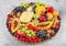 Fresh raw organic summer berries and exotic fruits in round large tray on light kitchen background. Papaya, grapes, nectarine,