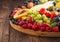 Fresh raw organic summer berries and exotic fruits in round large tray on wooden kitchen background. Papaya, grapes, nectarine,