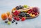 Fresh raw organic summer berries and exotic fruits in round wooden plate on light blue kitchen background. Papaya, grapes,